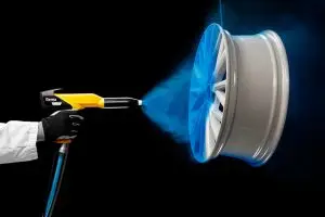 Technician applying blue powder coating to a metallic wheel rim using a spray gun