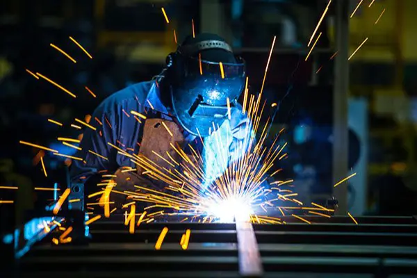 Welder wearing protective gear creating sparks while welding metal in an industrial workshop